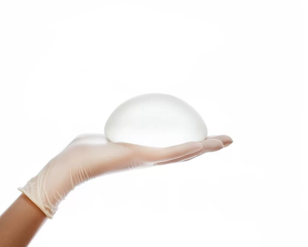 Round breast implant held on gloved hand