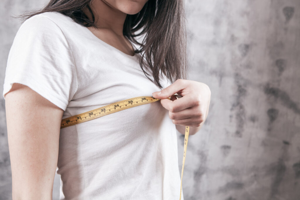 Woman measuring her breasts with a tape measure prior to breast implant sizing session